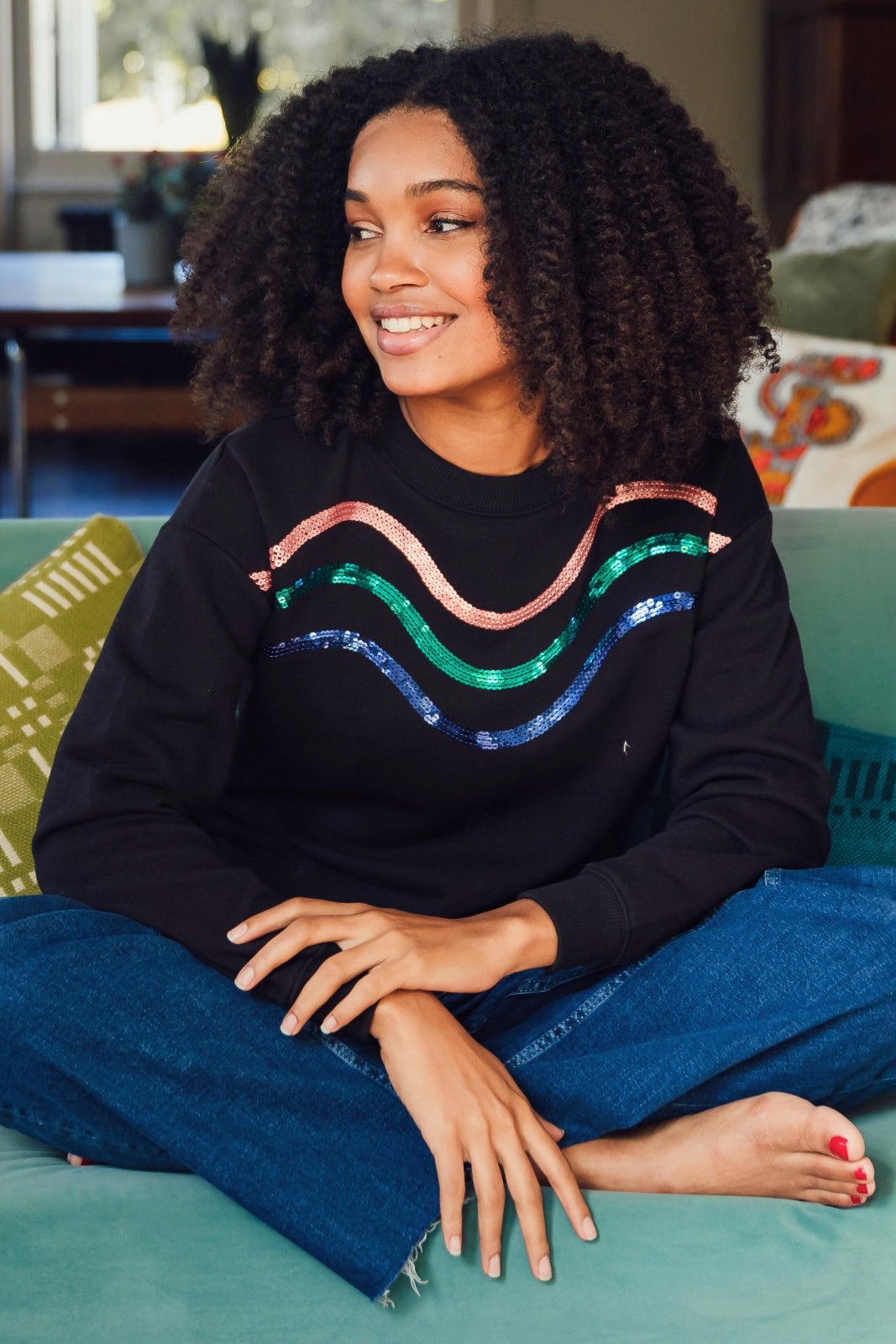 Woman wearing a black sweater with colorful patterns sitting on a couch.