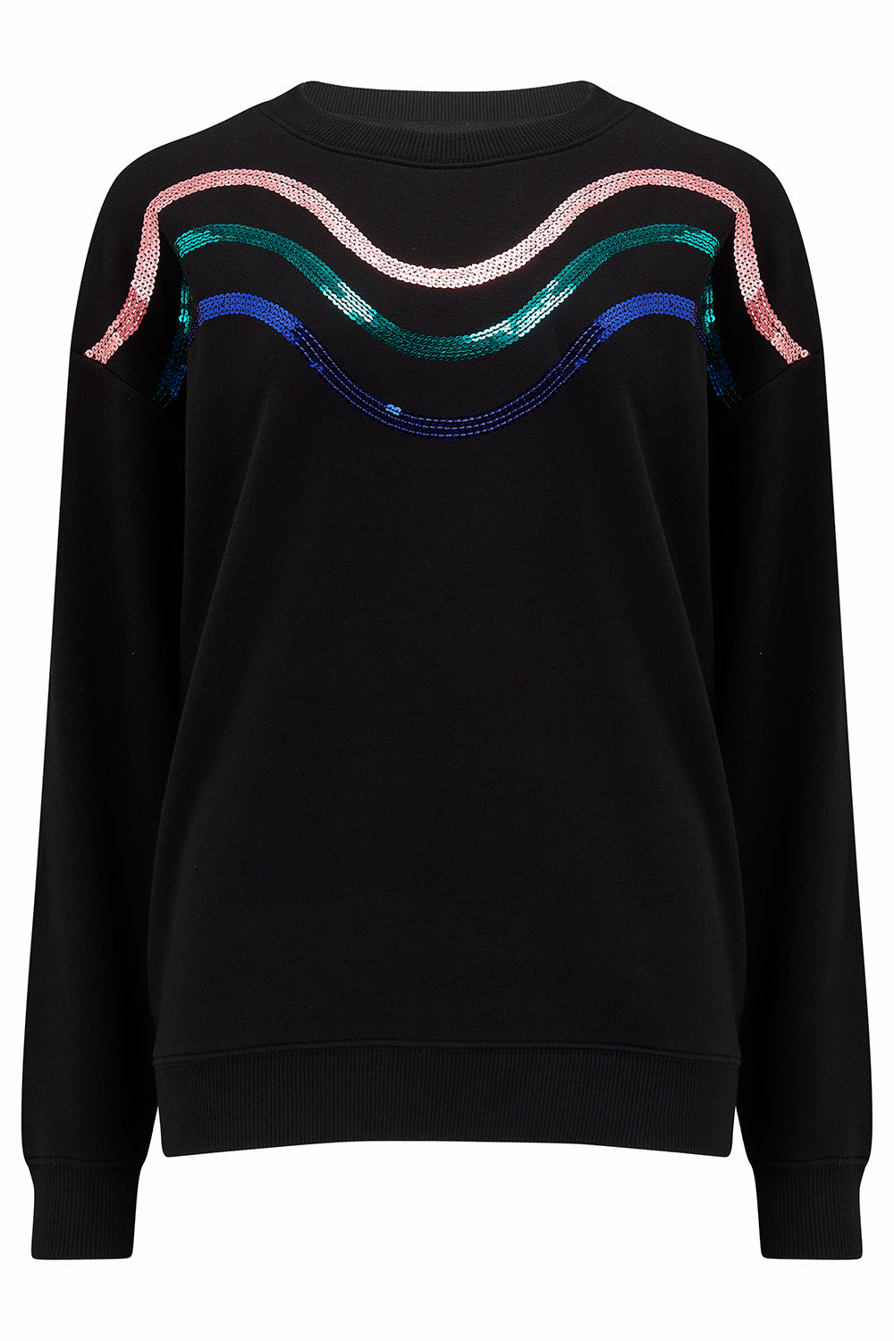 A woman standing, wearing a black sweatshirt with sequin waves in peach, emerald, and blue, and blue jeans.