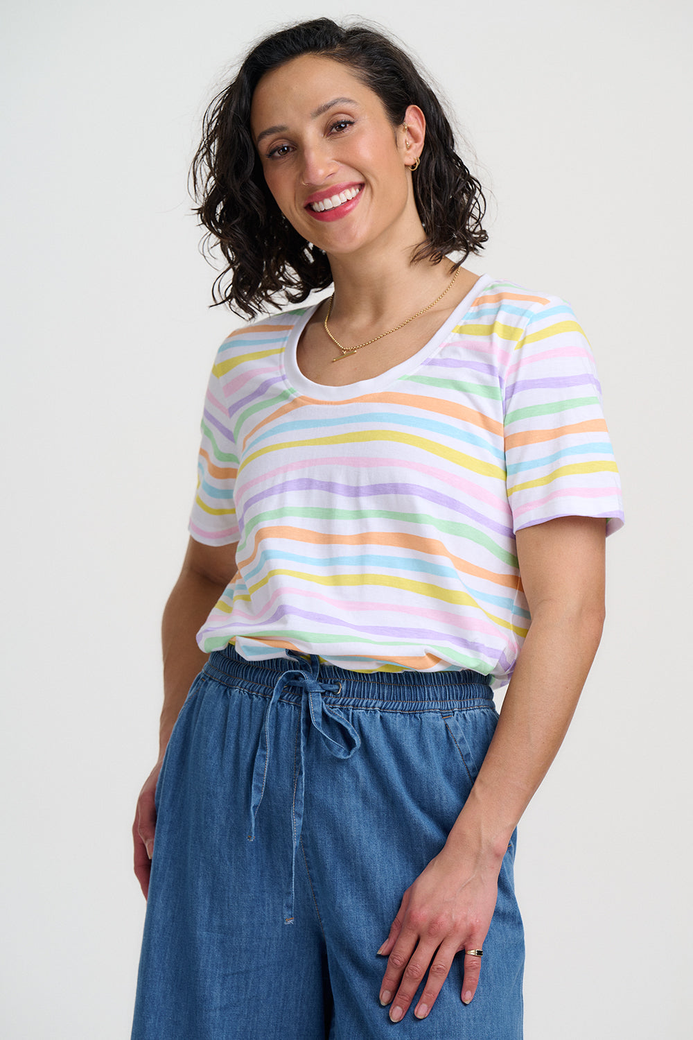 Woman wearing a colorful striped shirt and blue pants against a white background