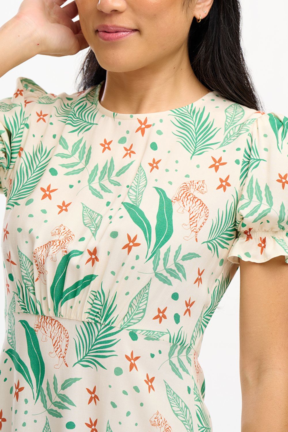 A model wearing a short-sleeved mini dress with a fitted waist and a frill hem skirt, featuring a jungle leaves print on a cream base.