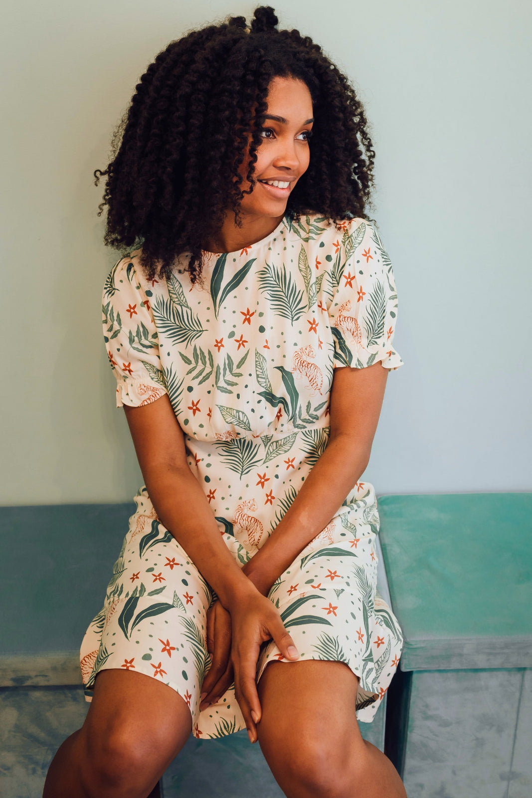 Woman wearing a floral dress sitting on a bench with a light blue wall in the background