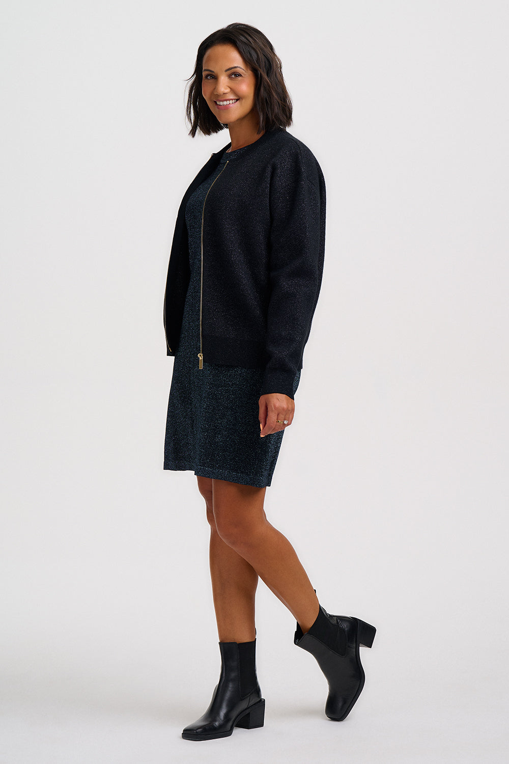 A woman modeling a dark navy blue zip-up cardigan and matching textured knit mini skirt set, paired with black ankle boots, against a plain light gray studio background.