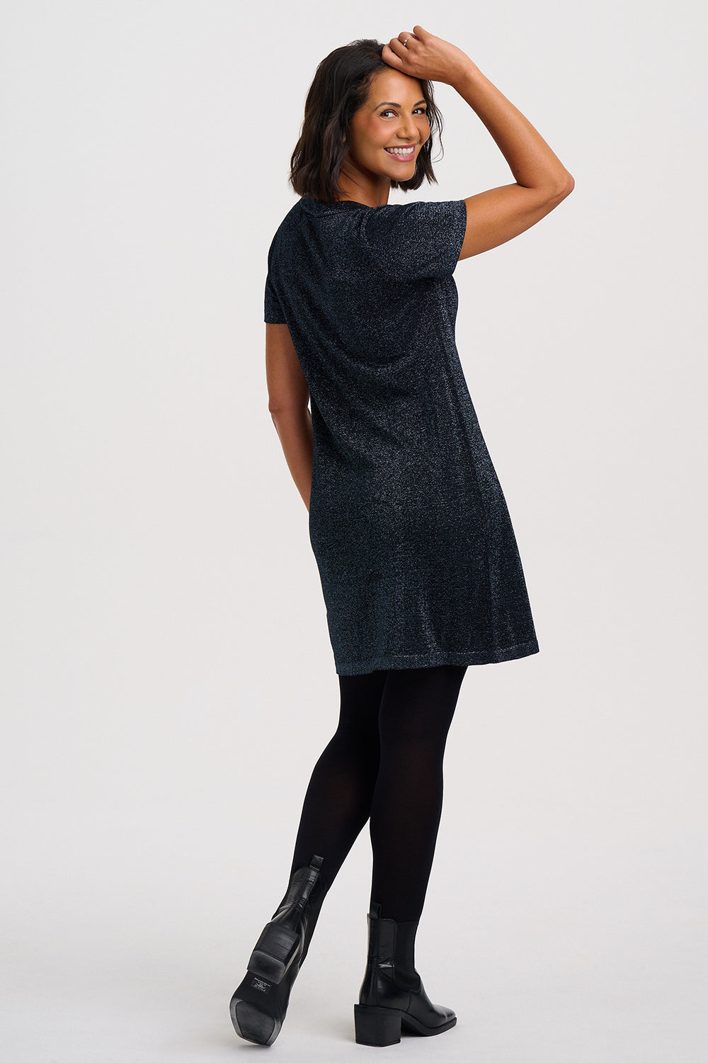 A woman modeling a short-sleeve, knee-length textured dress in a dark navy blue, shown from a side-back angle against a light gray studio background.