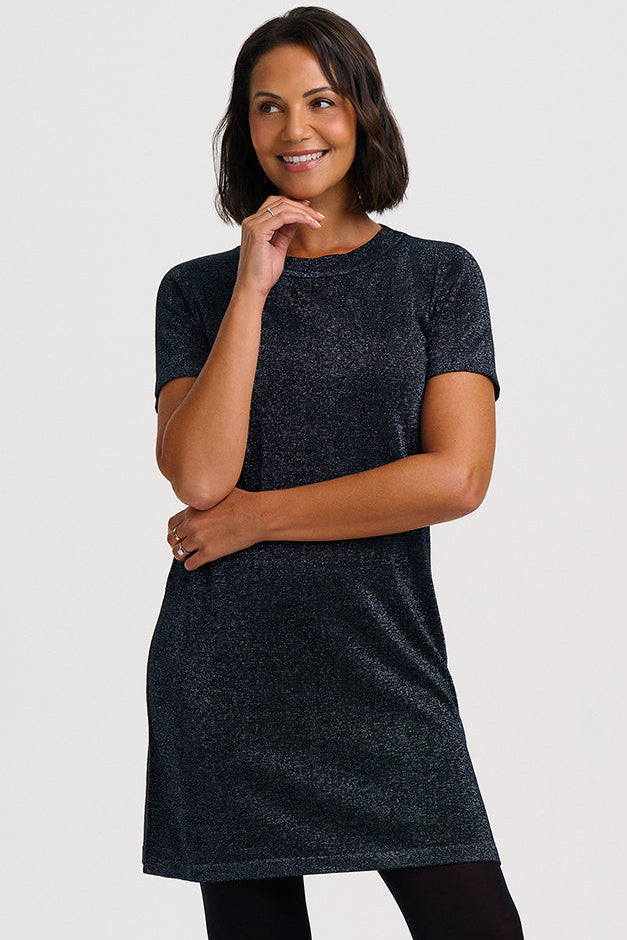 A woman modeling a short-sleeve dark gray knit dress with black tights and black ankle boots, standing against a light gray studio background.