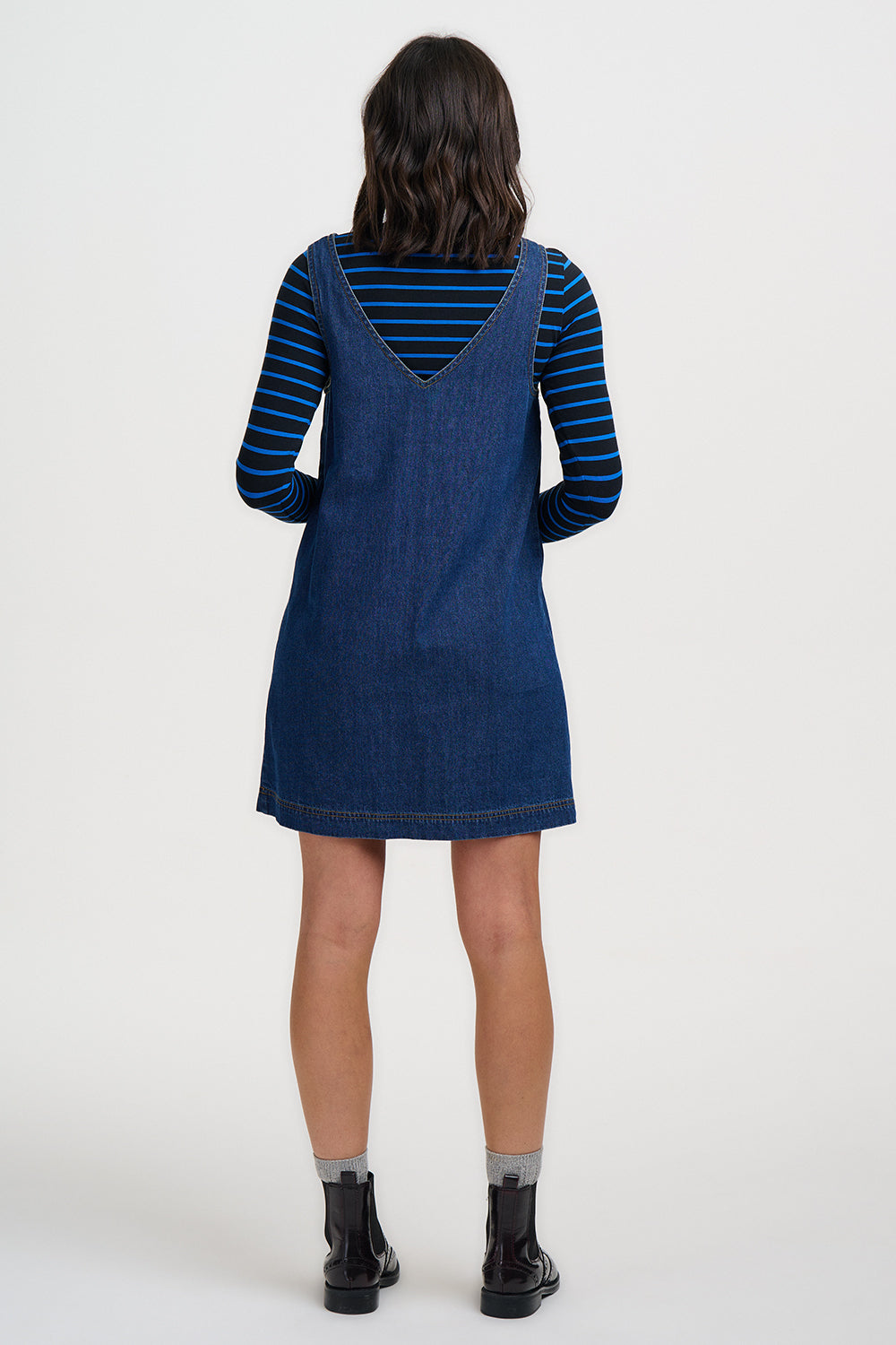 Person wearing a blue denim dress over a striped shirt on a white background