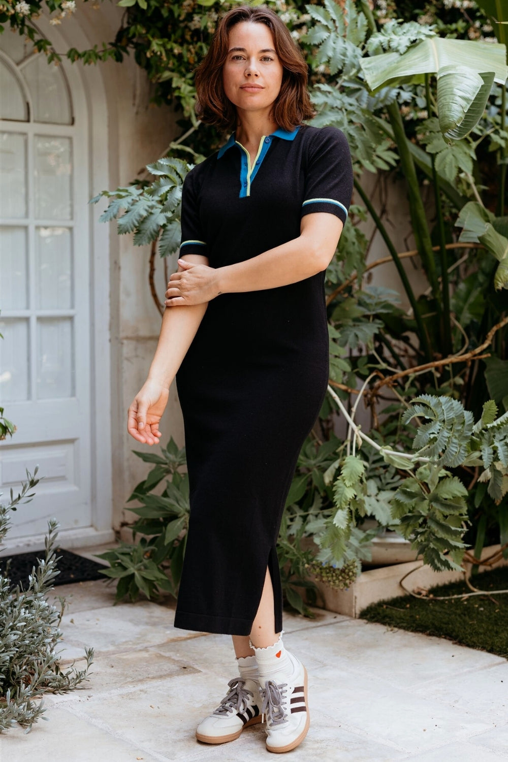 Woman in a black dress with white sneakers standing in front of greenery