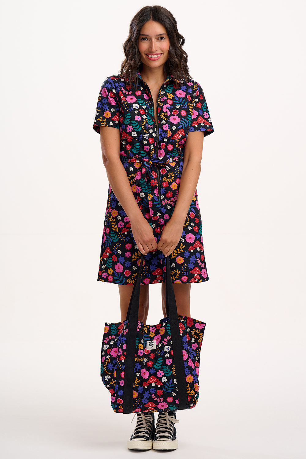 Woman wearing a colourful floral dress holding a matching bag on a white background