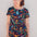 A model wearing a short-sleeved mini dress with a colorful jungle animal and foliage pattern on a black background.