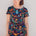 A model wearing a short-sleeved mini dress with a colorful jungle animal and foliage pattern on a black background.
