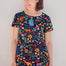 A model wearing a short-sleeved mini dress with a colorful jungle animal and foliage pattern on a black background.