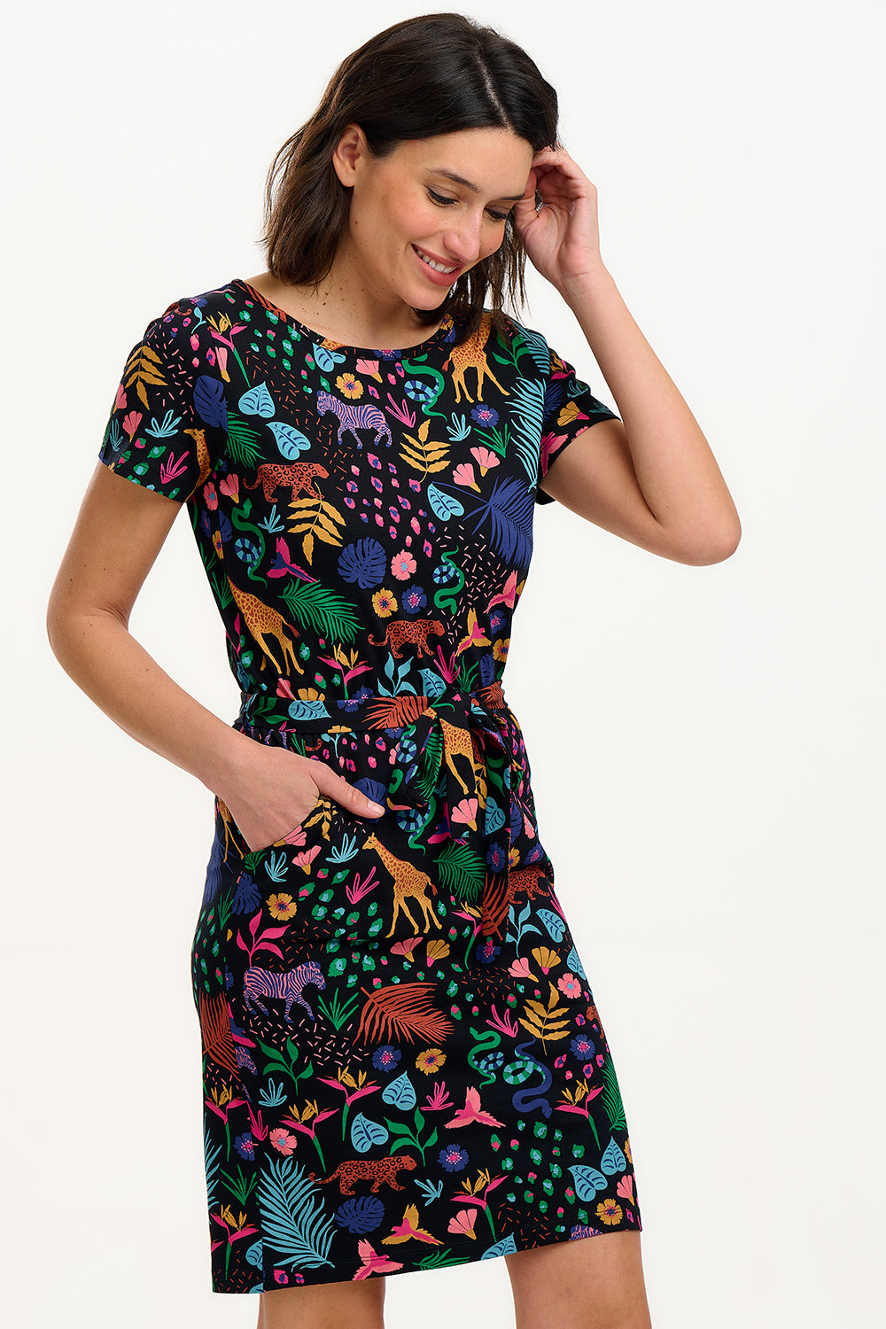 A model wearing a short-sleeved jersey mini dress with a black base and a colorful jungle spirit design, including various wildlife and foliage.