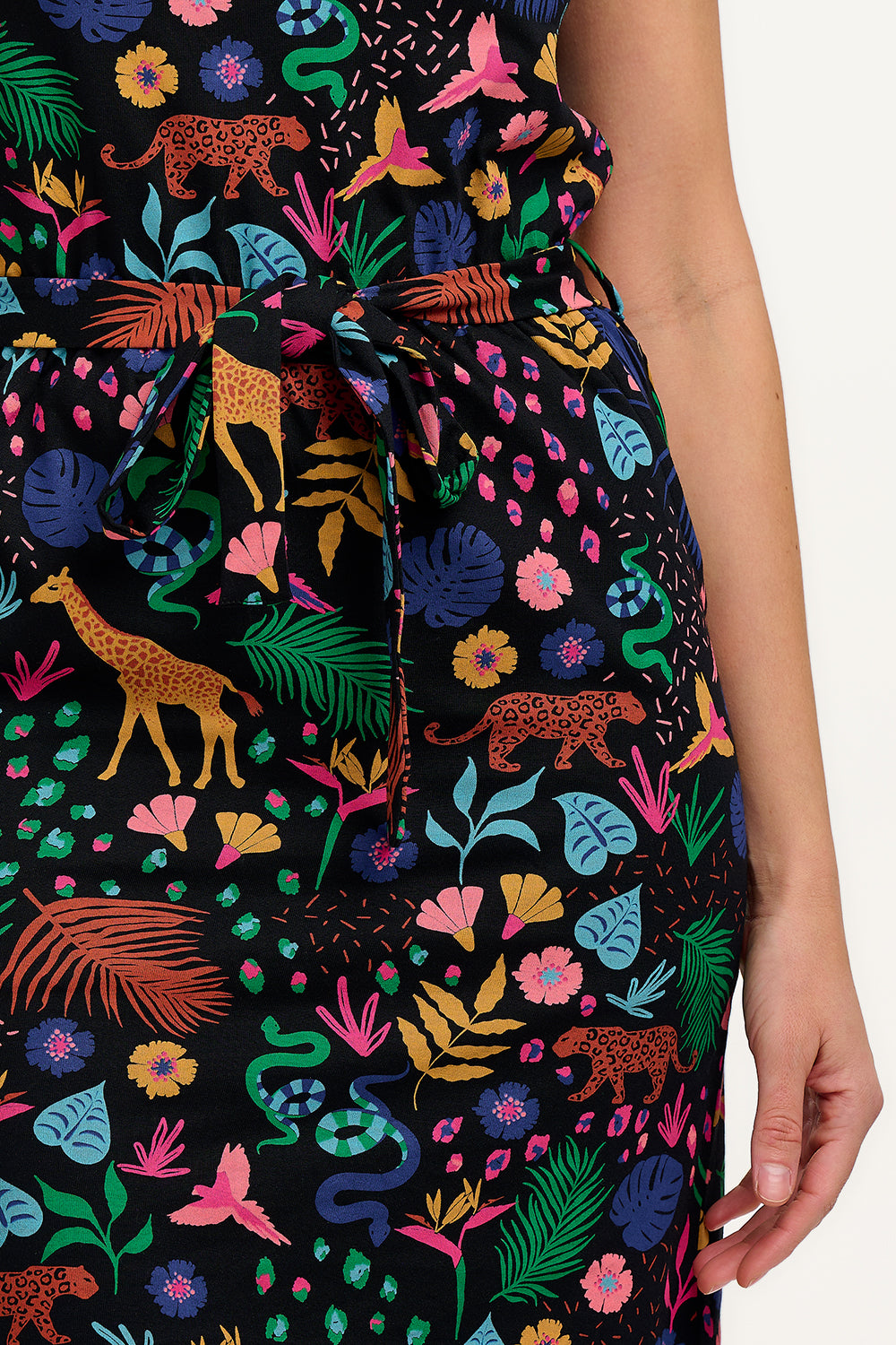 A model wearing a short-sleeved jersey mini dress with a black base and a colorful jungle spirit design, including various wildlife and foliage.