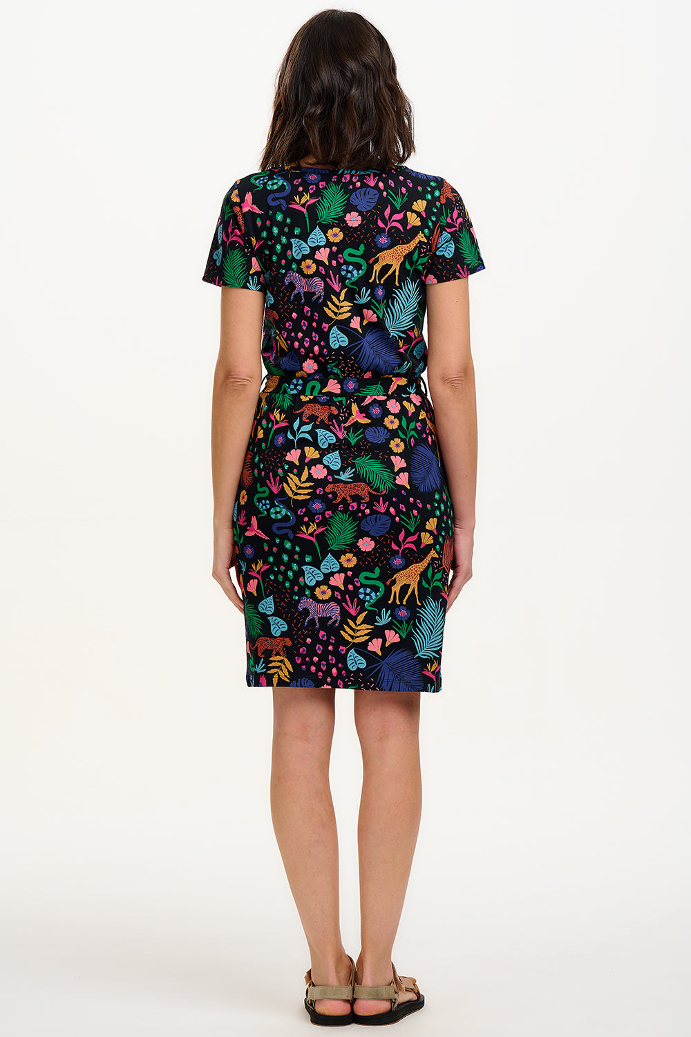 A model wearing a short-sleeved jersey mini dress with a black base and a colorful jungle spirit design, including various wildlife and foliage.