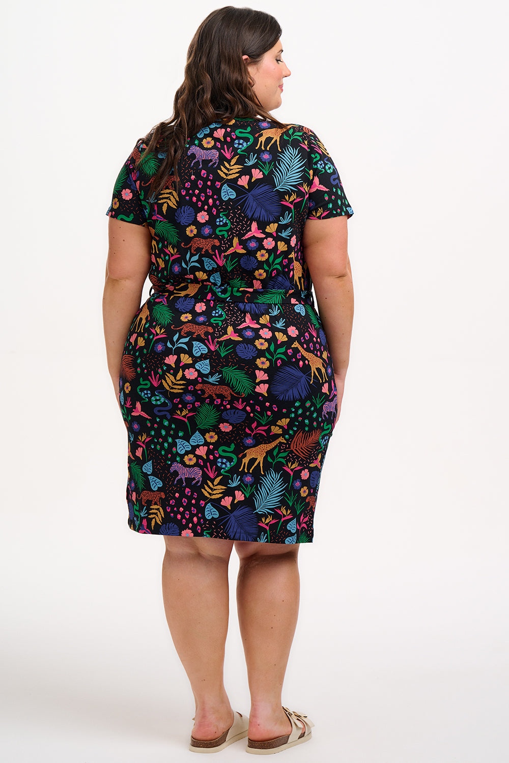 A model wearing a short-sleeved jersey mini dress with a black base and a colorful jungle spirit design, including various wildlife and foliage.