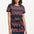 A model wearing a short-sleeved mini dress with a wavy chevron stripe pattern in black, teal, navy, tan, pink, and coral colors.