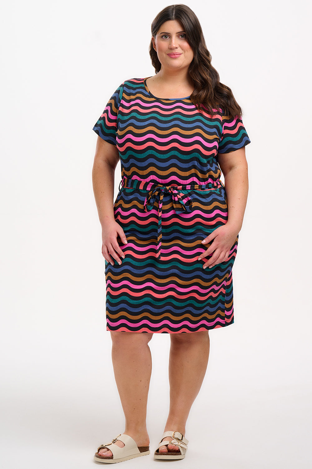 A model wearing a short-sleeved mini dress with a wavy chevron stripe pattern in black, teal, navy, tan, pink, and coral colors.