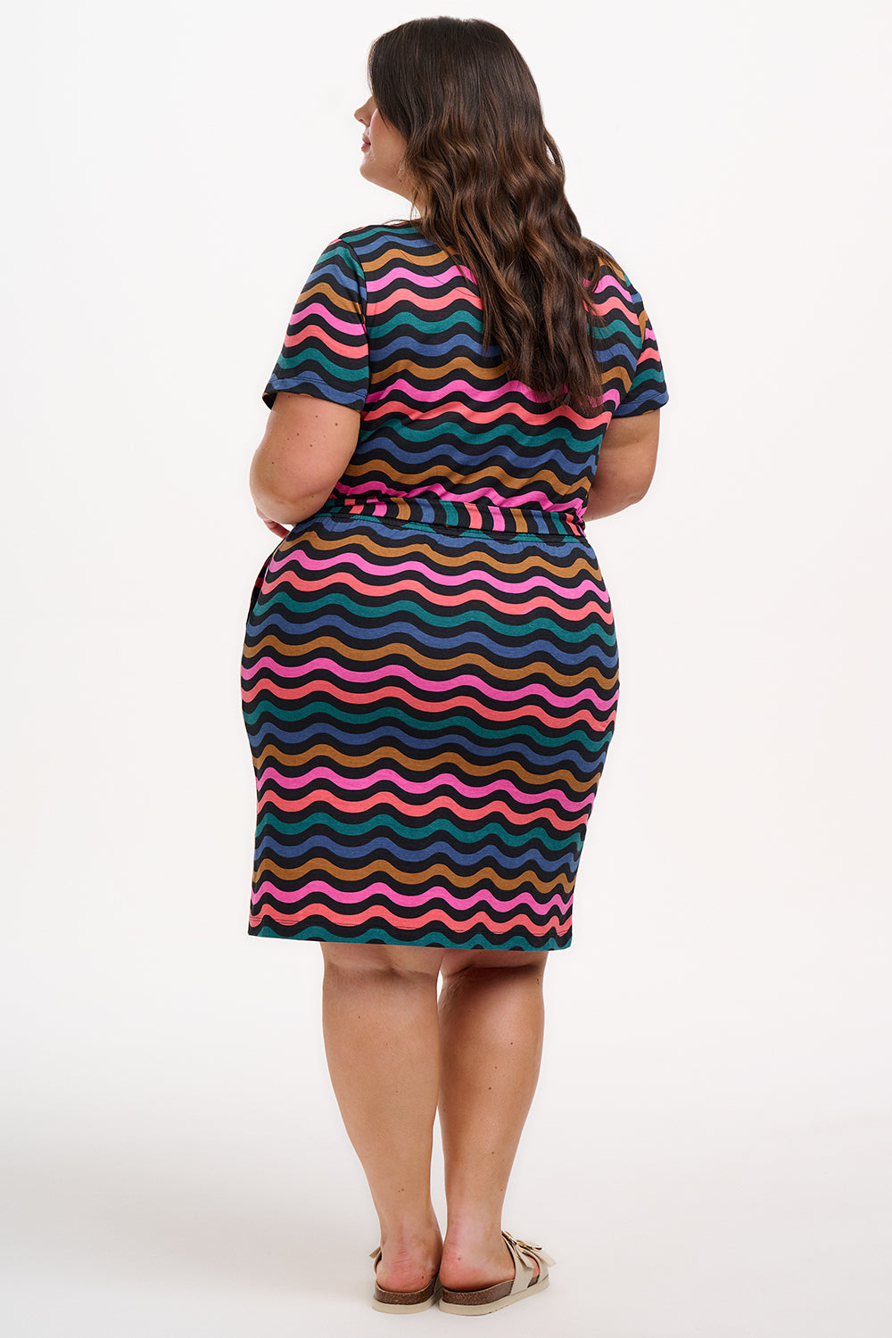 A model wearing a short-sleeved mini dress with a wavy chevron stripe pattern in black, teal, navy, tan, pink, and coral colors.