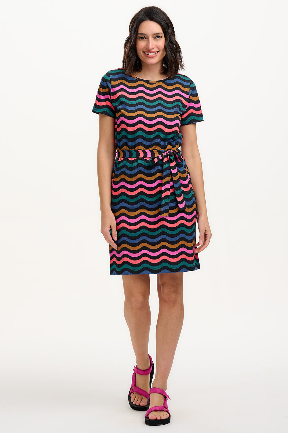 A model wearing a short-sleeved mini dress with a wavy chevron stripe pattern in black, teal, navy, tan, pink, and coral colors.