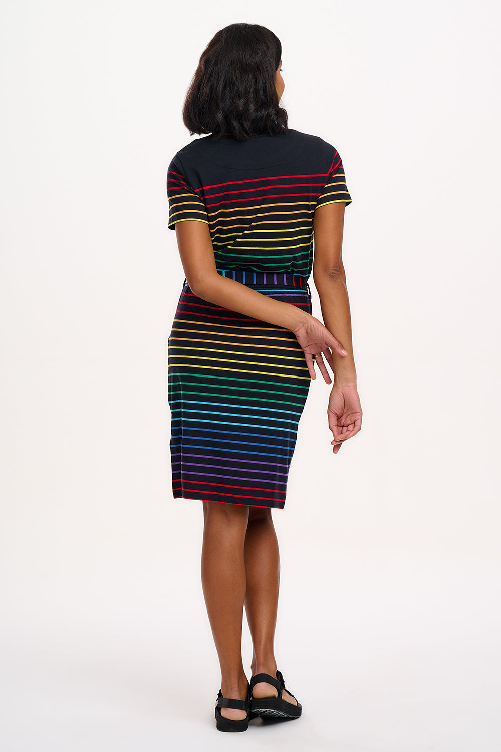 A model wearing a short-sleeved black mini dress with a colorful striped pattern and pockets
