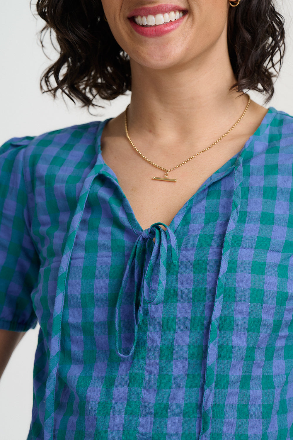 Woman wearing a green and blue checkered blouse with a necklace on a white background