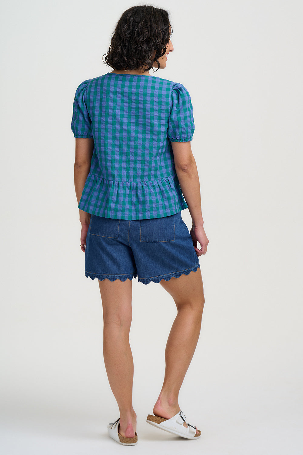 Woman wearing a blue checkered top and denim shorts on a white background