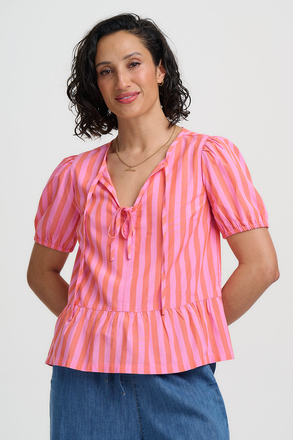 Woman wearing a pink and orange striped blouse with blue pants on a white background