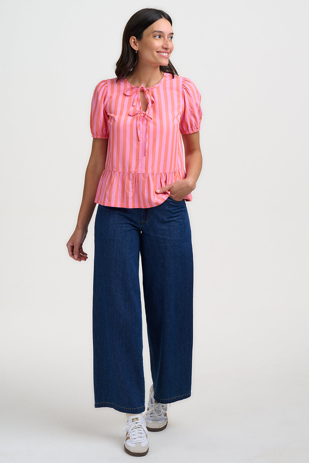 Woman wearing a pink striped blouse and blue jeans on a white background