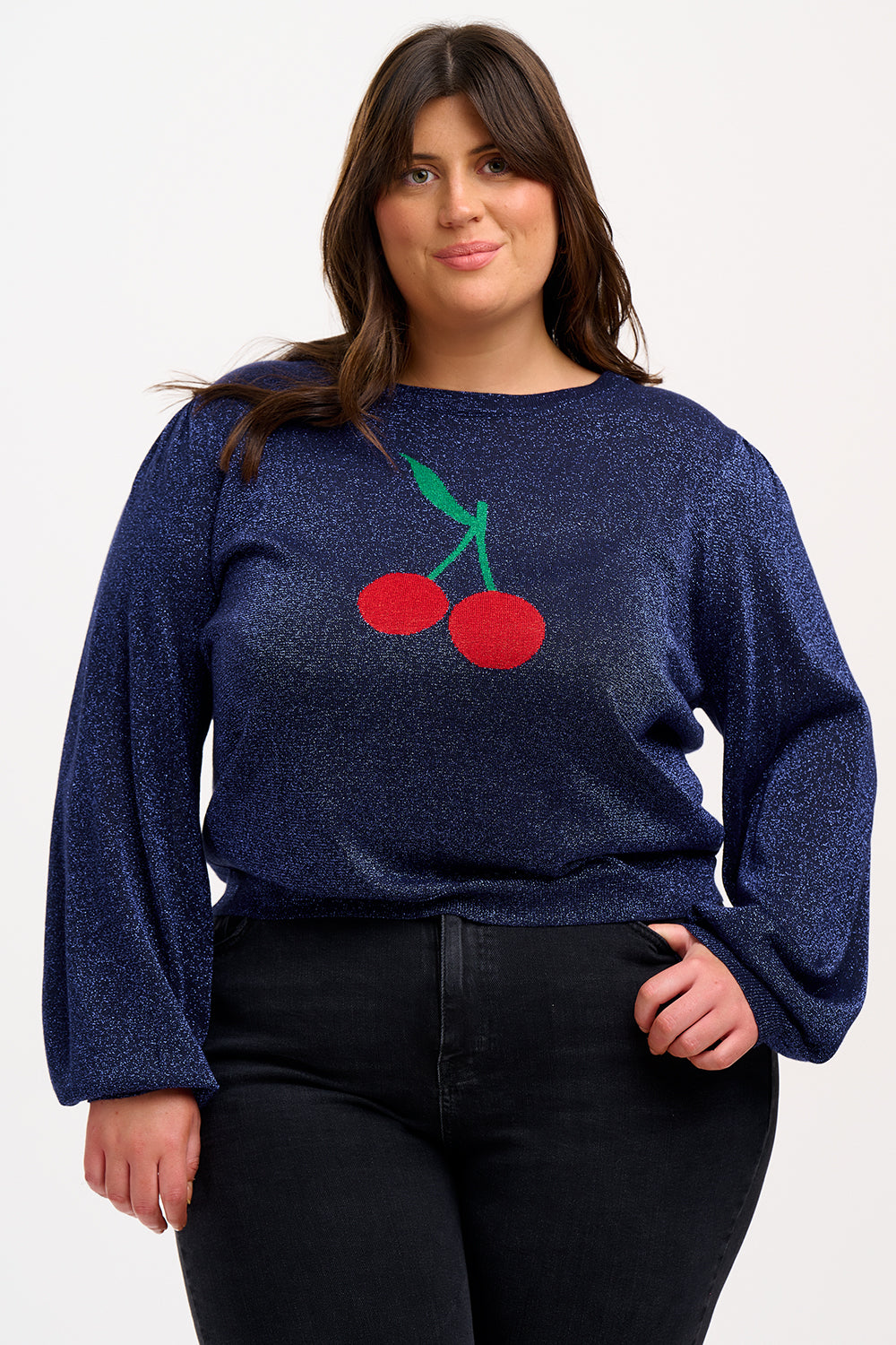 A woman wearing a navy blue jumper with a large red and green cherry motif on the front.