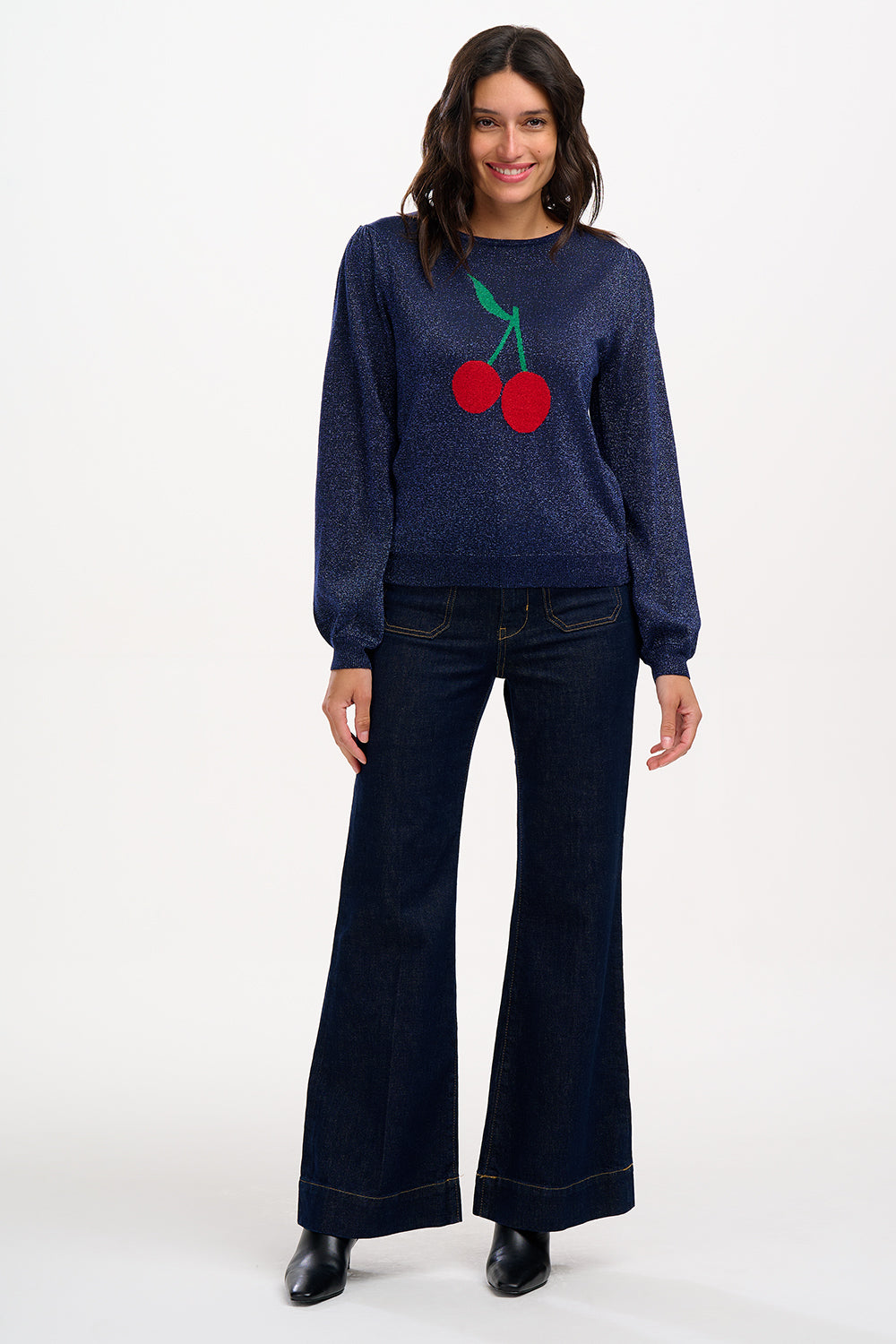 A woman wearing a navy blue jumper with a large red and green cherry motif on the front.