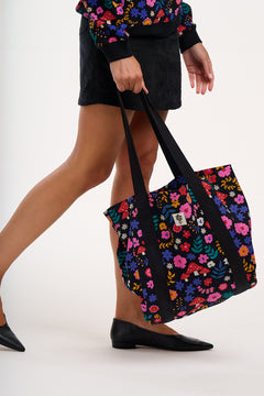 Person holding a black tote bag with colorful floral pattern on a white background
