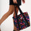 Person holding a black tote bag with colorful floral pattern on a white background