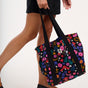 Person holding a black tote bag with colorful floral pattern on a white background