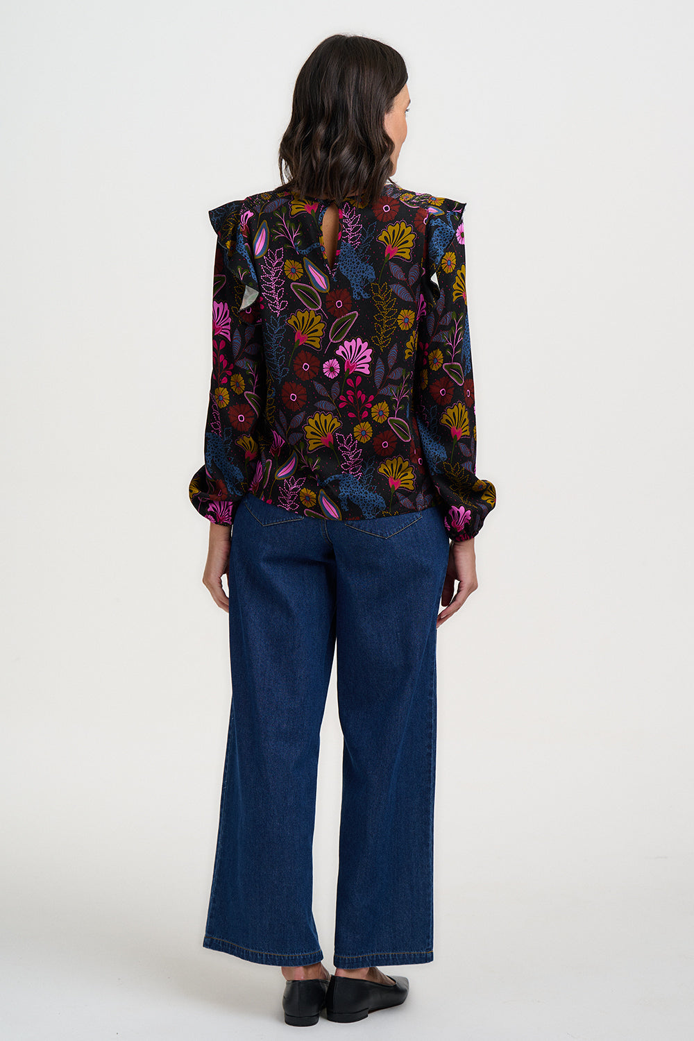 Person wearing a colorful floral blouse and blue pants on a white background