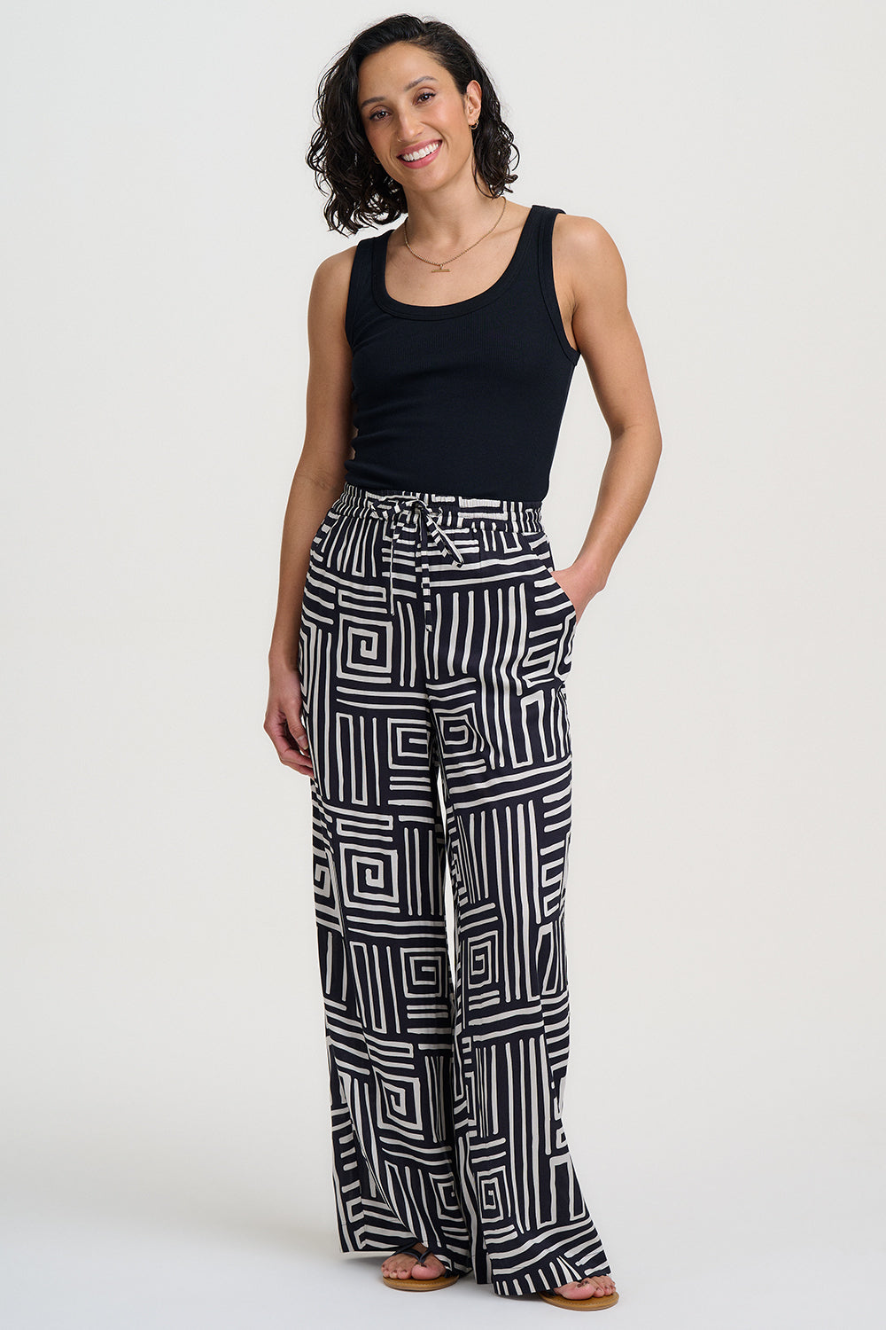 Woman wearing black tank top and geometric patterned pants on a white background