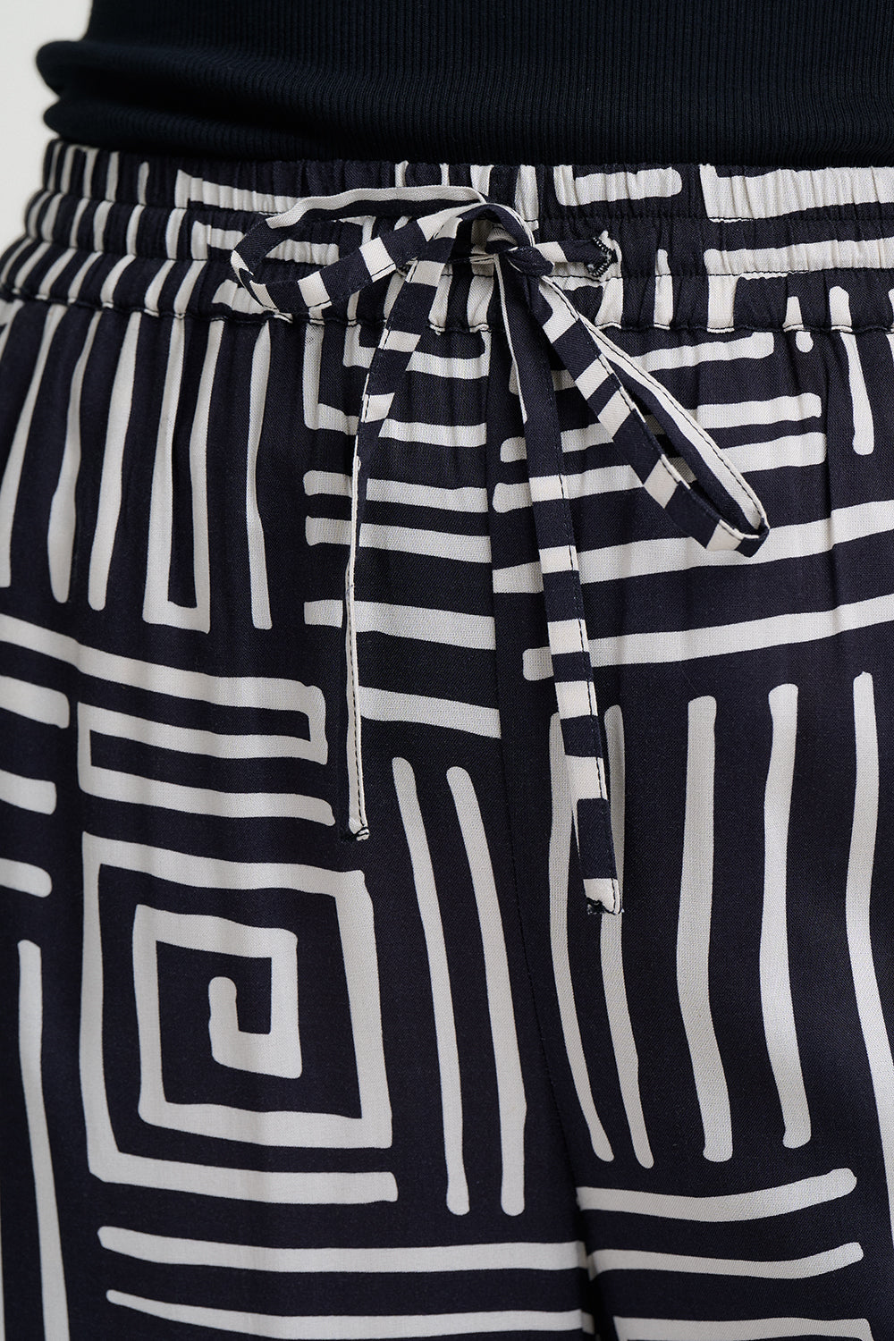 Black and white geometric patterned pants with a tie waist on a plain background