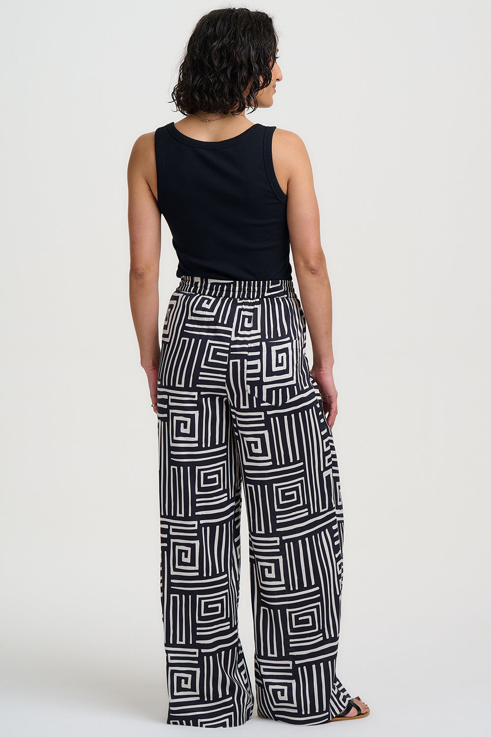 Person wearing a black sleeveless top and geometric patterned pants on a white background