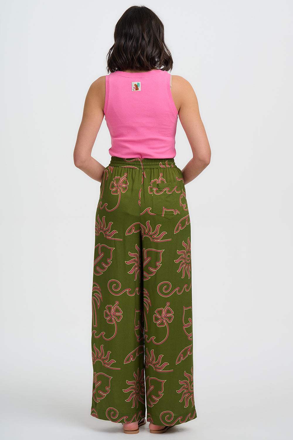 Person wearing a pink sleeveless top and green patterned pants on a white background