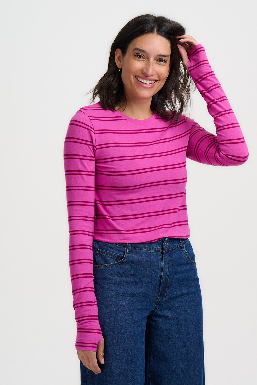 Woman wearing a pink striped long-sleeve top and blue jeans on a white background