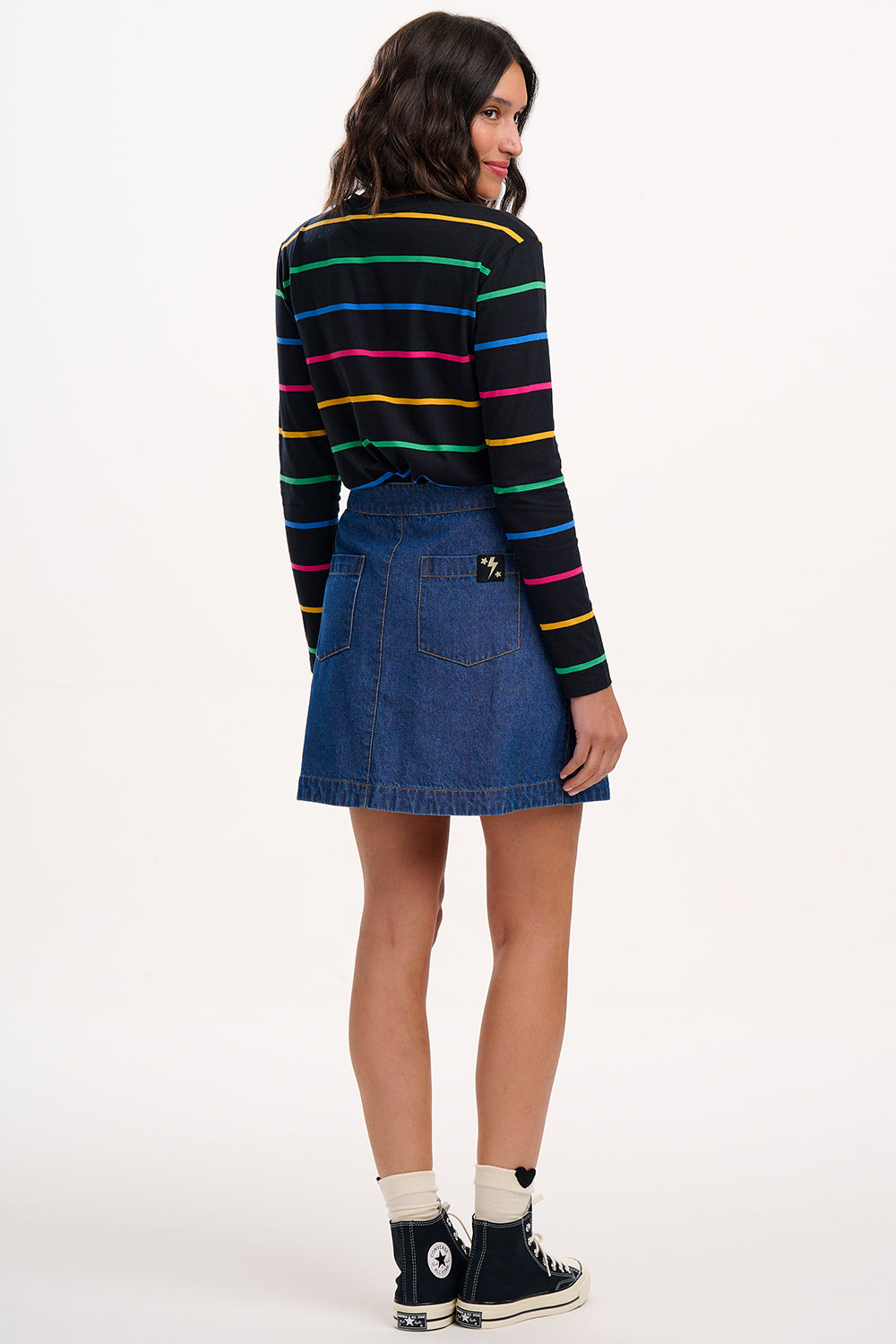 Sugarhill Brighton model wearing a colorful striped sweater and denim skirt on a white background