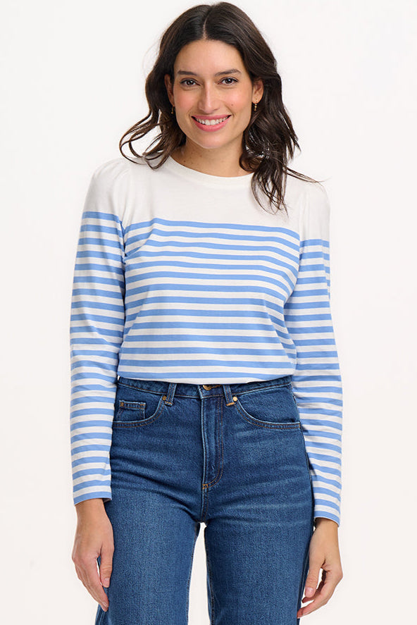 A woman wearing an off-white jersey top with horizontal French blue and off-white stripes, paired with blue jeans.