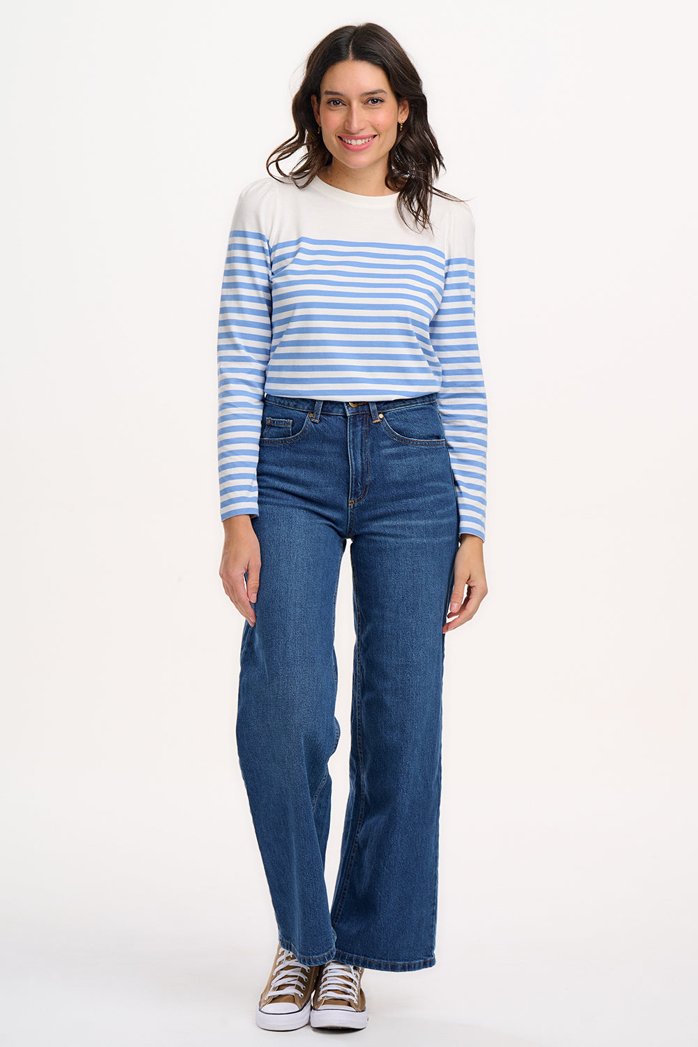 A woman wearing an off-white jersey top with horizontal French blue and off-white stripes, paired with blue jeans.