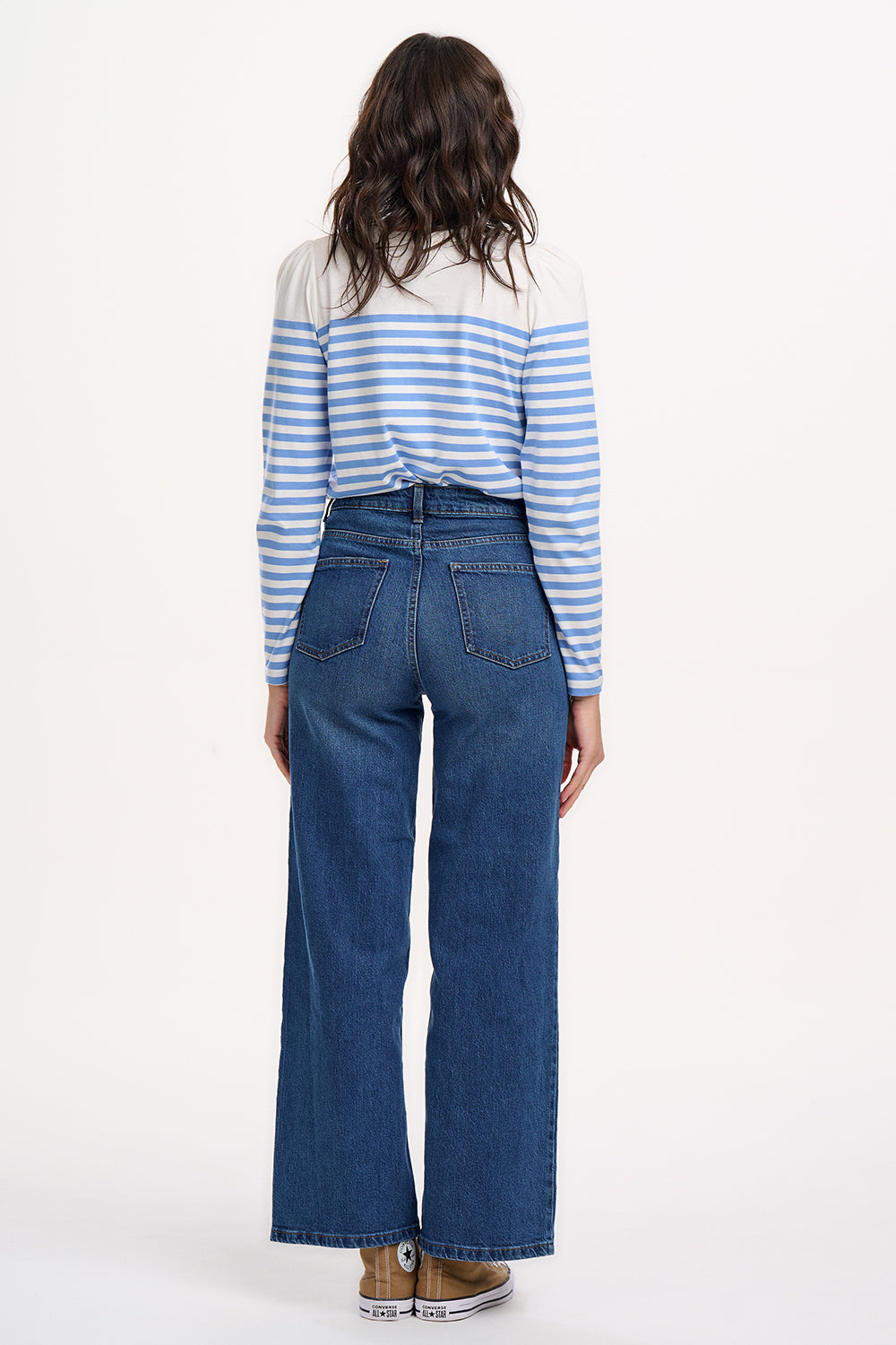 A woman wearing an off-white jersey top with horizontal French blue and off-white stripes, paired with blue jeans.