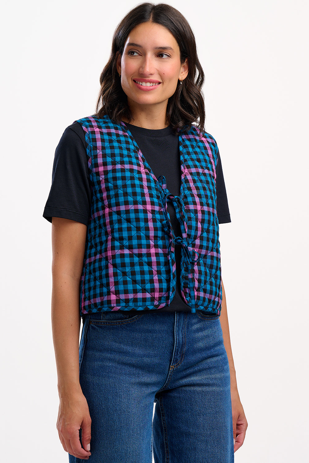 Woman wearing a black t-shirt with a blue and pink plaid vest on a white background