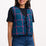 Woman wearing a black t-shirt with a blue and pink plaid vest on a white background