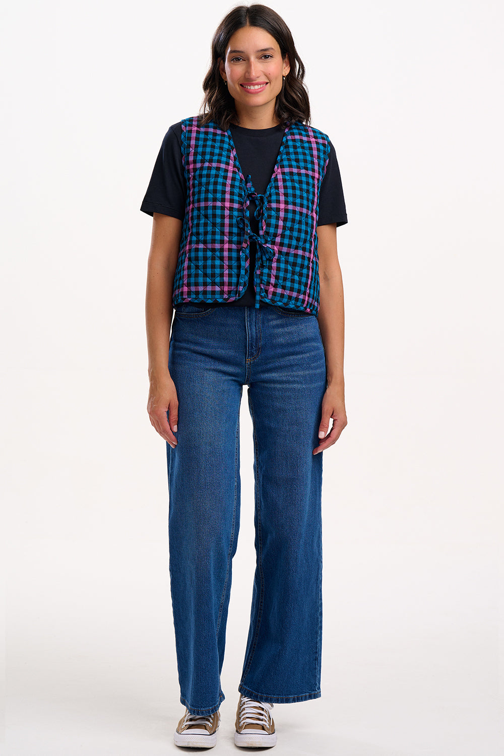 Woman wearing a plaid vest over a black shirt with blue jeans on a white background
