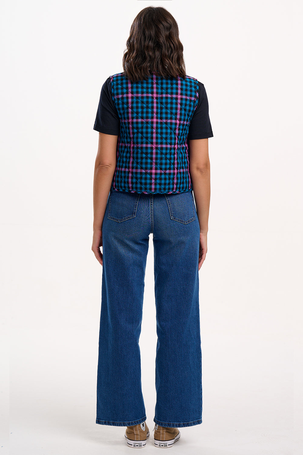 Person wearing a plaid vest over a black shirt and blue jeans on a white background