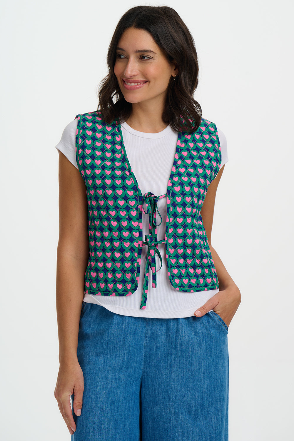 Woman wearing a patterned vest over a white shirt and blue pants on a white background