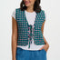 Woman wearing a patterned vest over a white shirt and blue pants on a white background