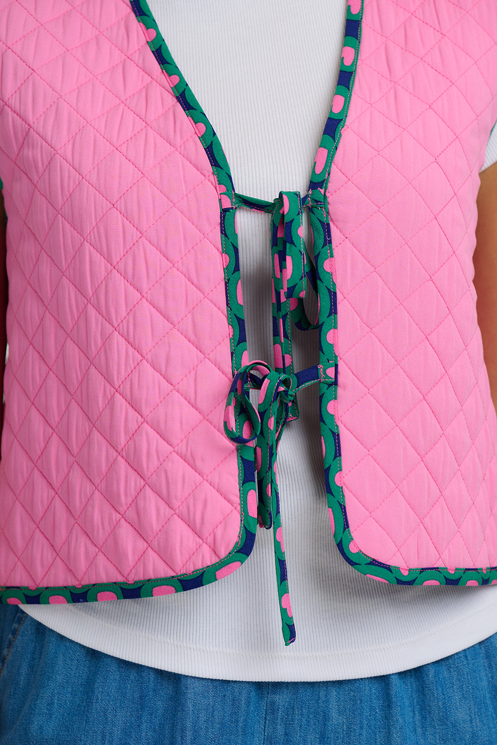 Pink quilted vest with green and pink patterned tie on a white background