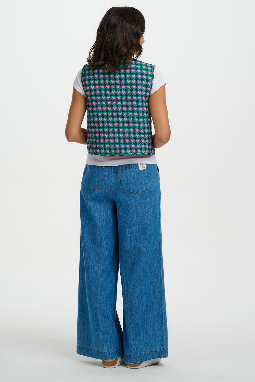 Person wearing a patterned vest and blue jeans on a white background